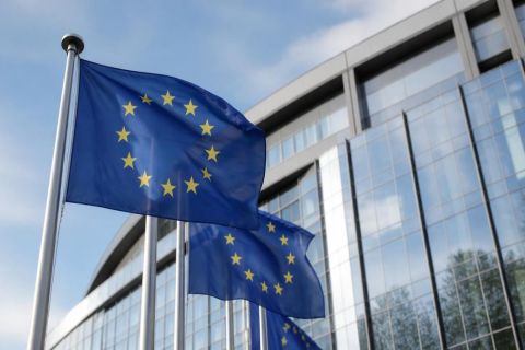 Drapeau européen flottant devant un bâtiment institutionnel vitré, illustration de la réglementation européenne sur l’intelligence artificielle